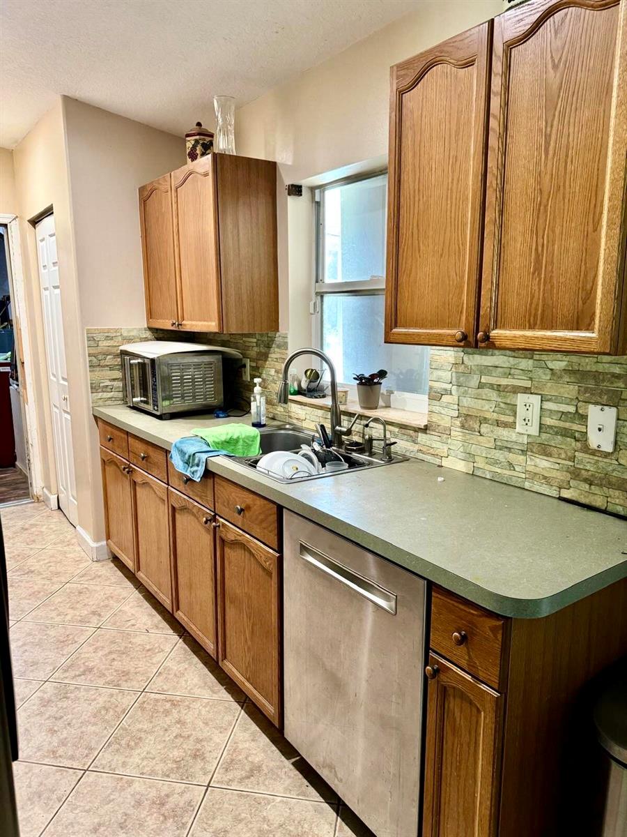 A kitchen features oak cabinets, a green laminate countertop, a stainless dishwasher, and stone backsplash — 16298 90th Street N, FL 33470, FL