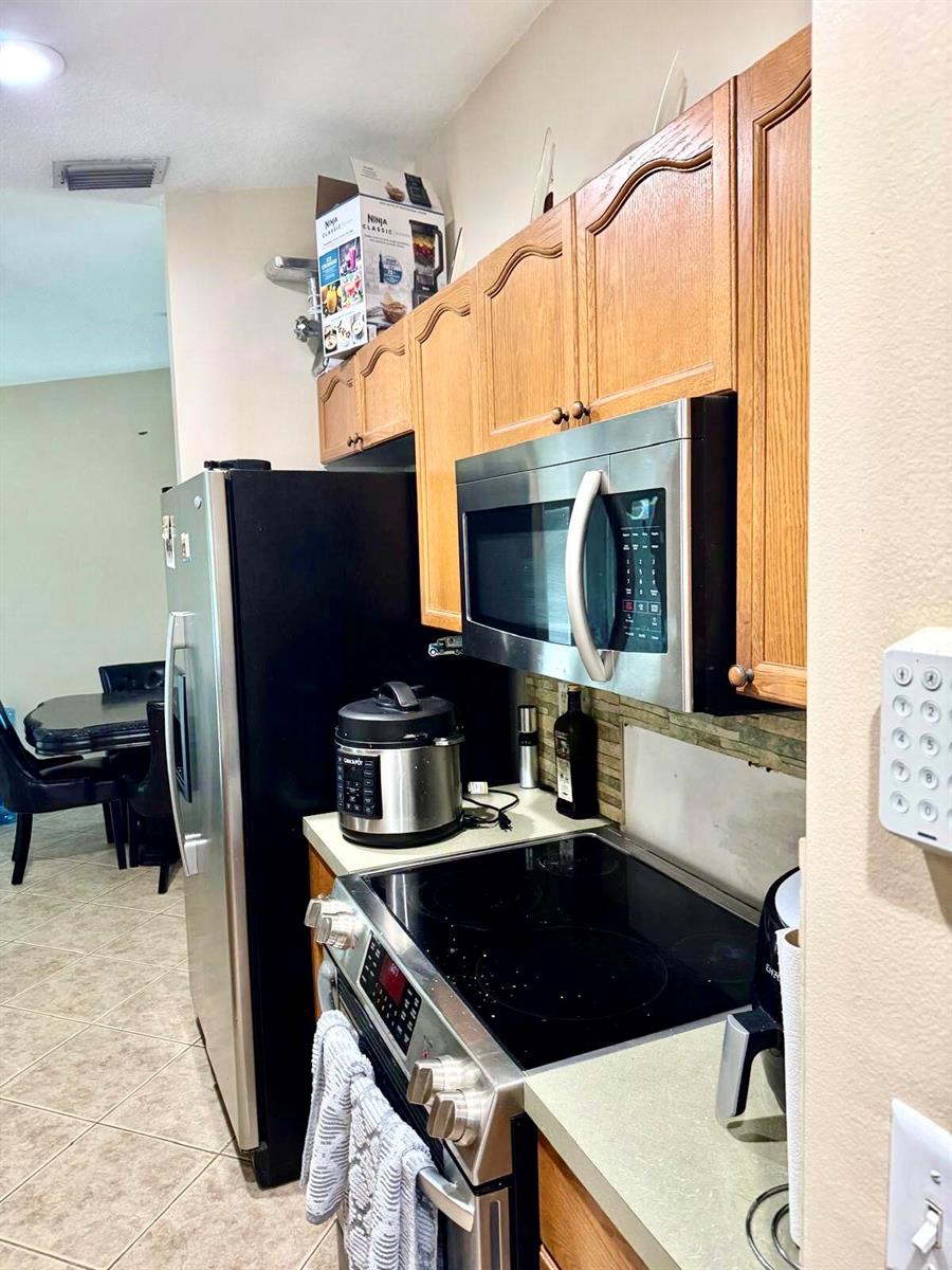 A kitchen features wood cabinets, stainless steel appliances, a black refrigerator, and a tile floor — 16298 90th Street N, FL 33470, FL