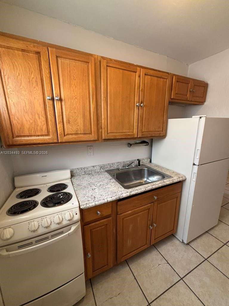 A small kitchen features wooden cabinets, a white stove, a sink, and a refrigerator — 14120 NW 24th Ct # 204, Opa-Locka FL 33054, OPA-LOCKA, FL