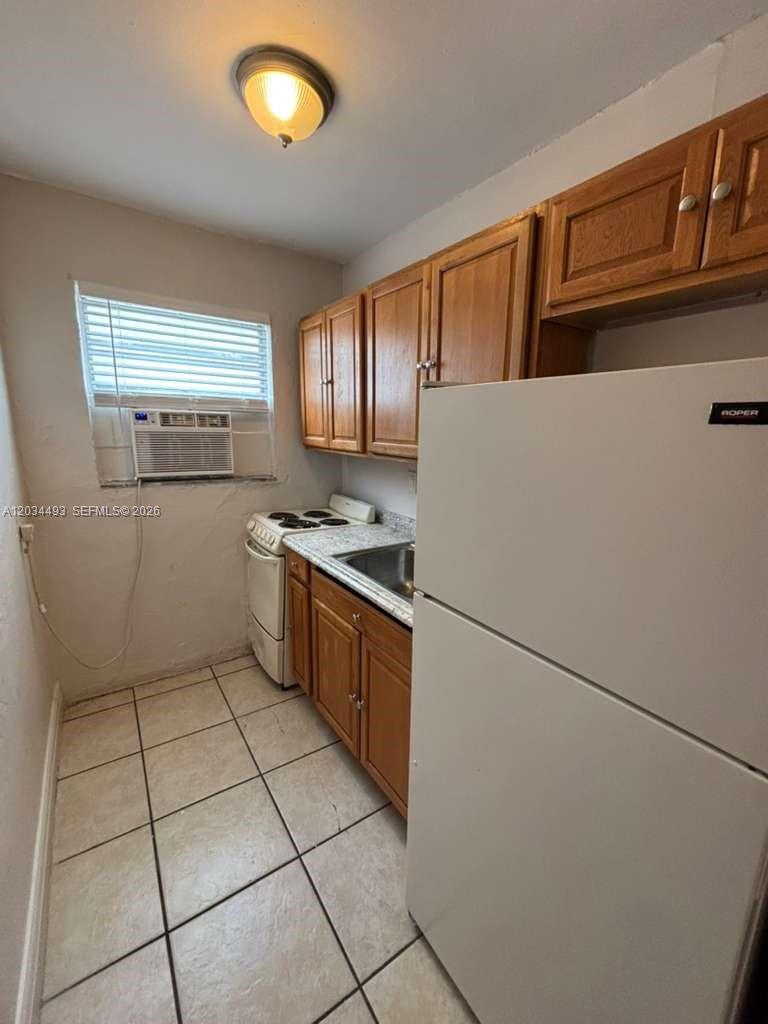 A small kitchen features wooden cabinets, a white refrigerator, a stove, and tiled flooring — 14120 NW 24th Ct # 204, Opa-Locka FL 33054, OPA-LOCKA, FL