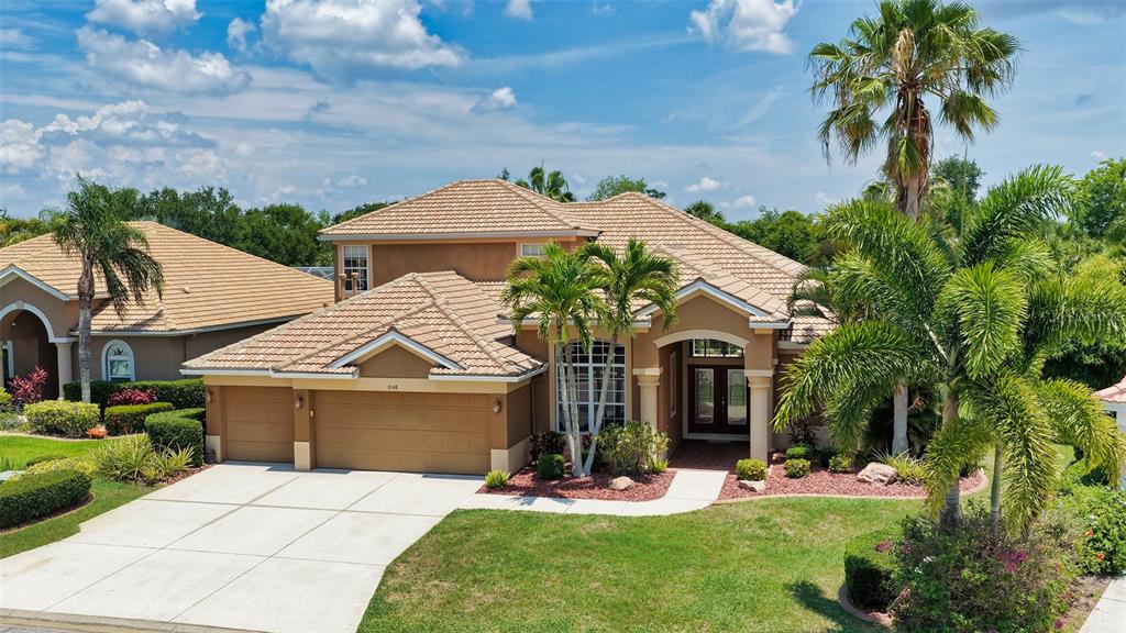 A two-story tan house with a tiled roof, a three-car garage, and palm trees — 6148 PALOMINO CIRCLE, BRADENTON, FL