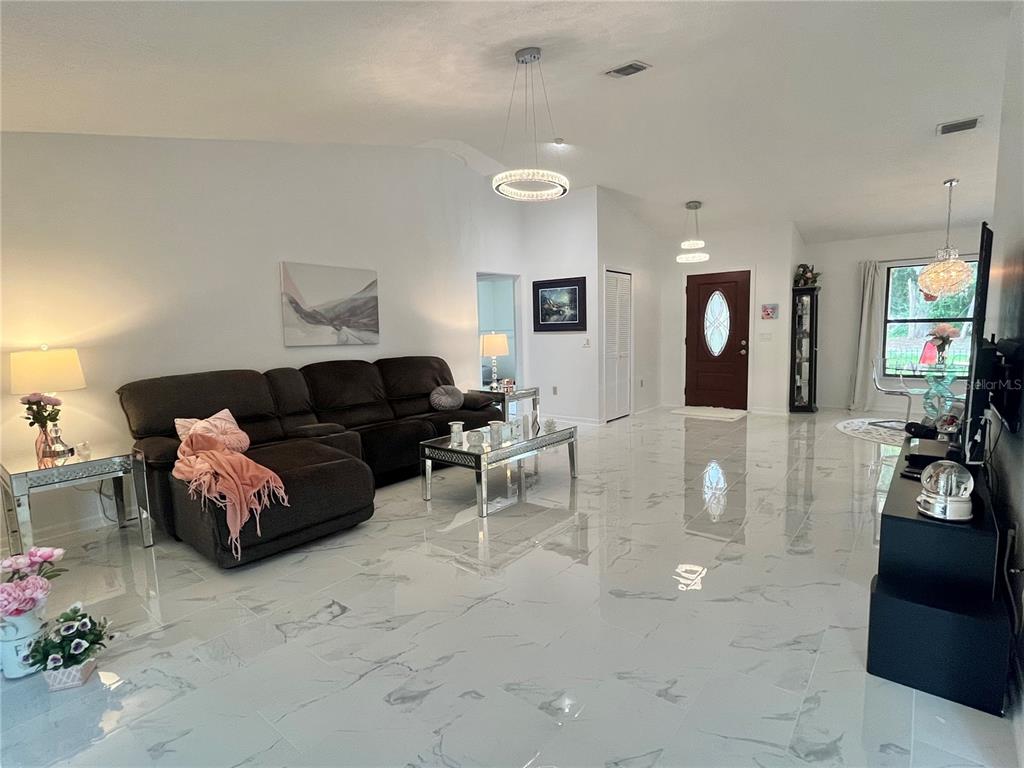 A living room features white marble-look tile flooring, a dark sofa, and modern pendant lighting — 35049 SILVER OAK DRIVE, LEESBURG, FL