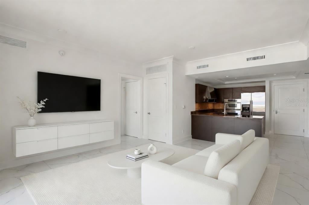A living room with white walls, marble floors, a wall-mounted TV, and an open kitchen — 1350 MAIN STREET UNIT 707, SARASOTA, FL
