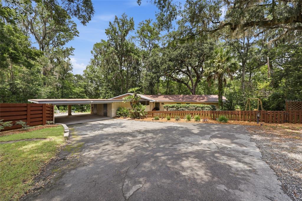 A single-story house with a carport and wooden fence sits behind a large cracked driveway — 1732 NW 8TH AVENUE, GAINESVILLE, FL
