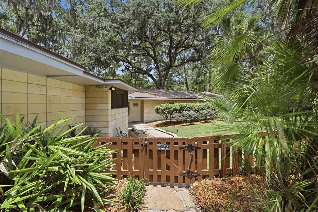 A wooden gate opens to a stone walkway leading to a light-colored brick house exterior — 1732 NW 8TH AVENUE, GAINESVILLE, FL