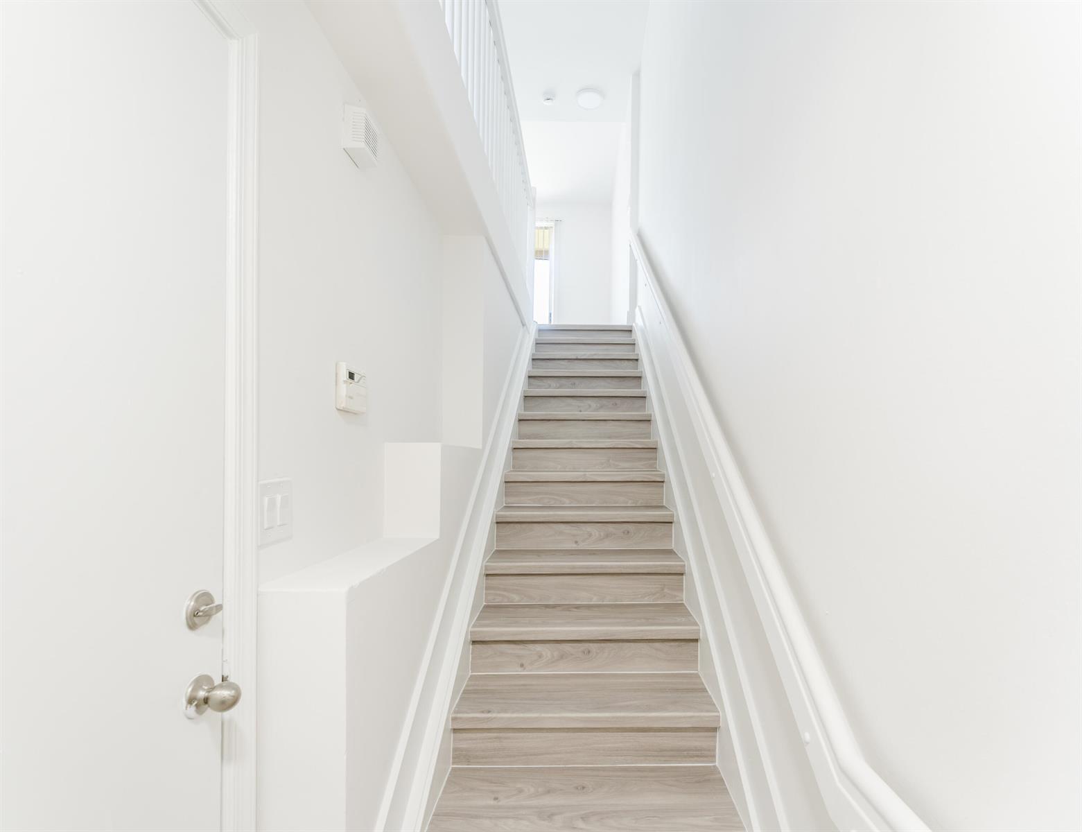 A staircase with light wood-look steps leads upward between two plain white walls — 20889 Saint Andrews Boulevard, Boca Raton FL 33433, BOCA RATON, FL