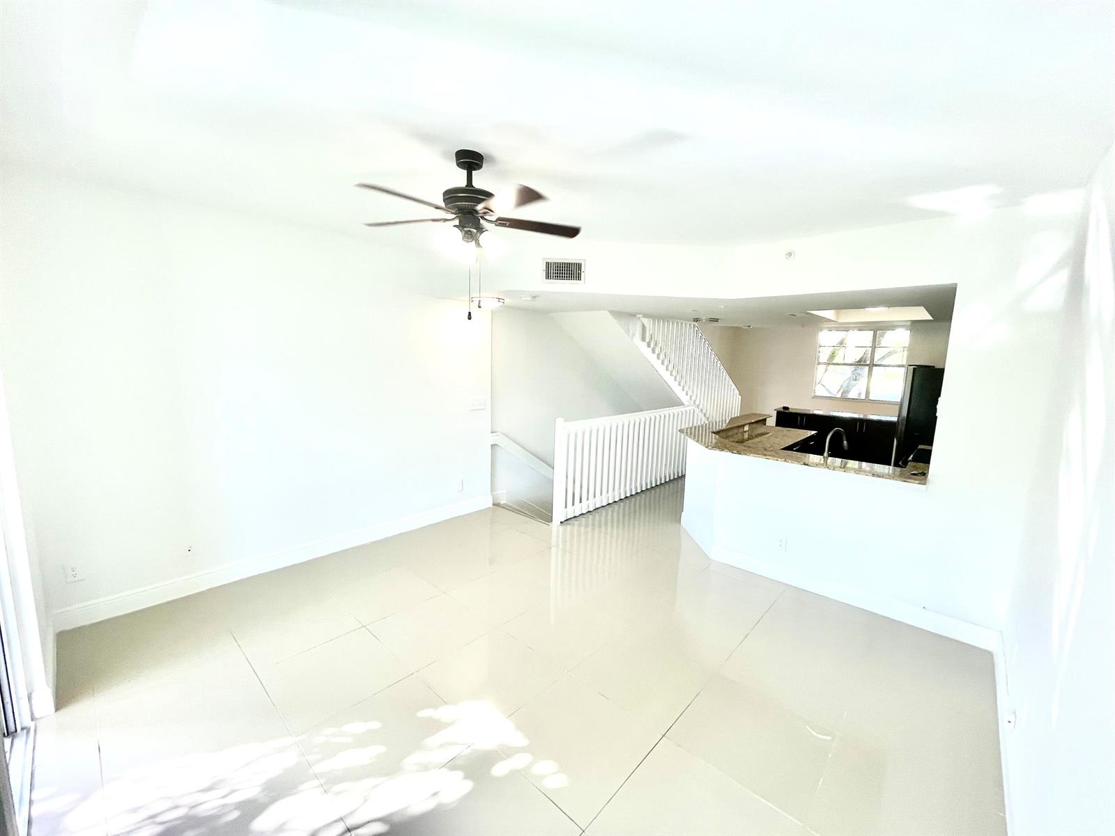 An open-concept living area features white tile floors, a ceiling fan, and a kitchen peninsula — 20889 Saint Andrews Boulevard, Boca Raton FL 33433, BOCA RATON, FL