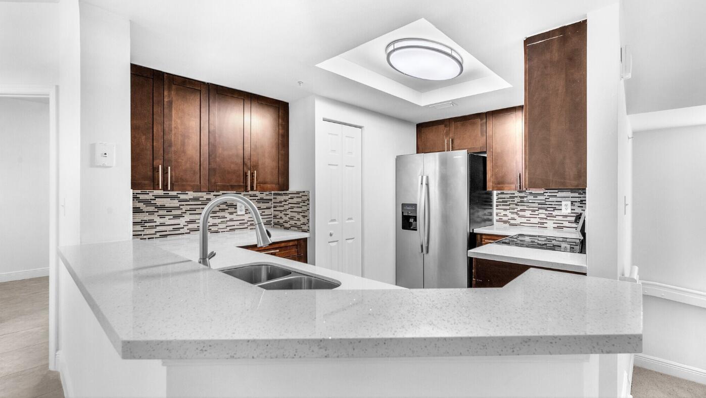 A kitchen features dark wood cabinets, a light quartz countertop, and a stainless steel refrigerator — 20889 Saint Andrews Boulevard, Boca Raton FL 33433, BOCA RATON, FL
