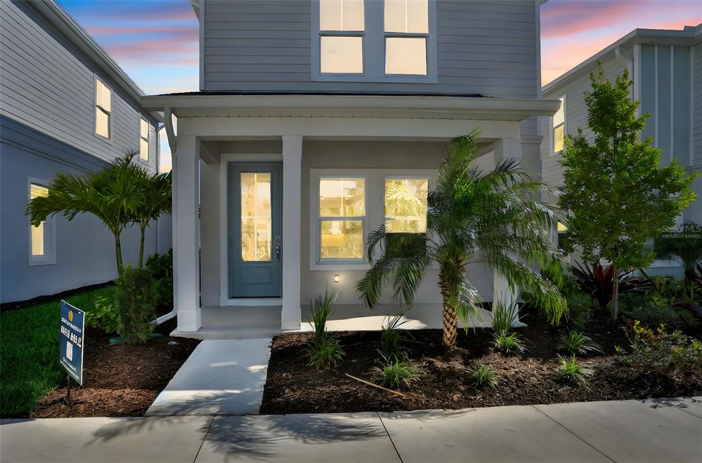 The exterior of a two-story house features a covered front porch and a small garden — 9084 CORMACK LANE, LAKEWOOD RANCH, FL