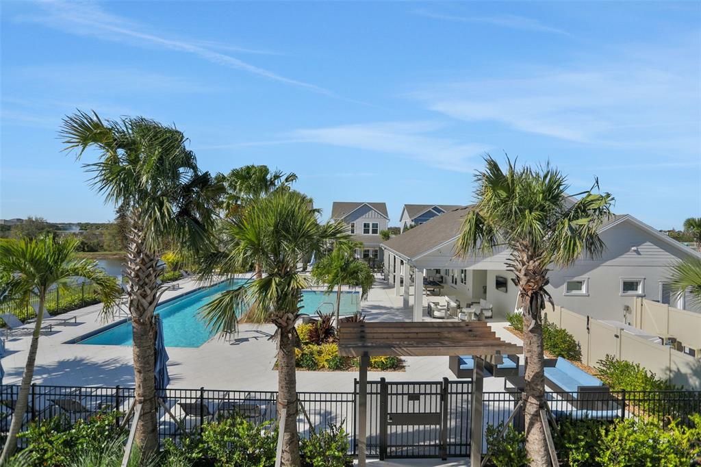 An outdoor swimming pool area with palm trees, a covered patio, and a metal fence — 9084 CORMACK LANE, LAKEWOOD RANCH, FL