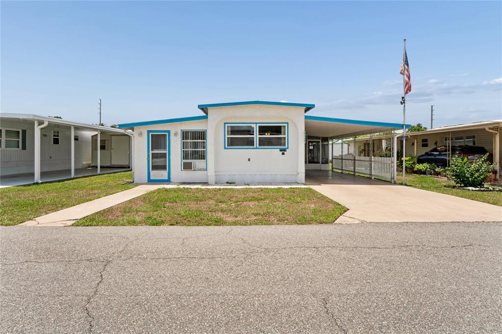 A single-story mobile home with a carport, white siding, and blue trim under a clear sky — 38618 REMORA AVENUE UNIT 92, ZEPHYRHILLS, FL