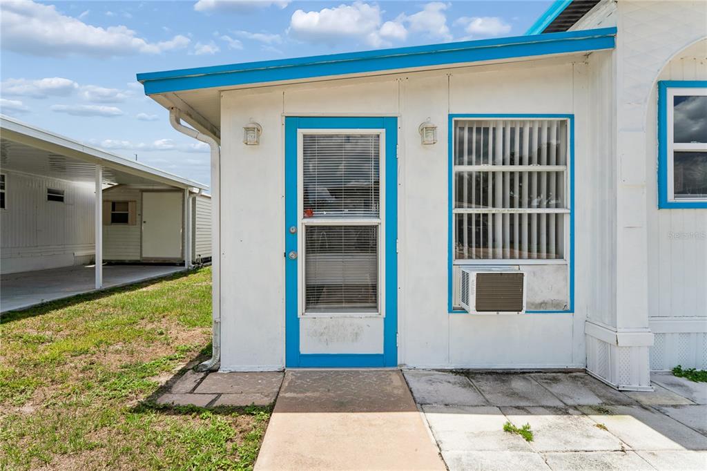 A white mobile home exterior features a blue-trimmed door, a window, and a window air conditioner — 38618 REMORA AVENUE UNIT 92, ZEPHYRHILLS, FL