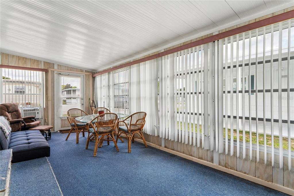A sunroom features blue carpeting, wood-paneled walls, vertical blinds, and a glass-topped dining set — 38618 REMORA AVENUE UNIT 92, ZEPHYRHILLS, FL