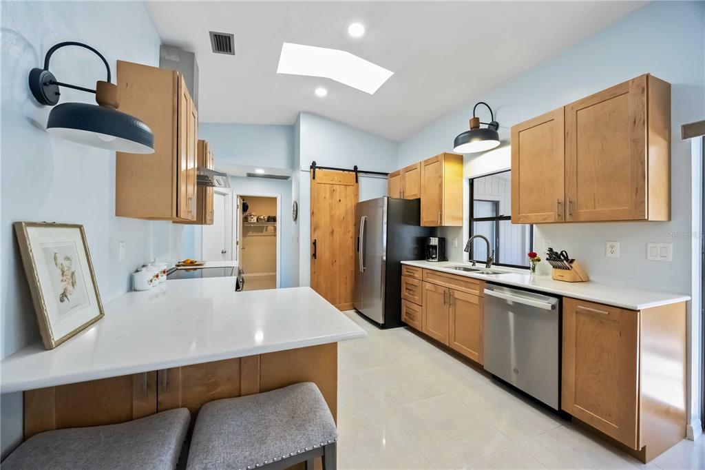 A kitchen features light wood cabinets, white countertops, stainless steel appliances, and a sliding barn door — 17341 HOLMES AVENUE, PORT CHARLOTTE, FL