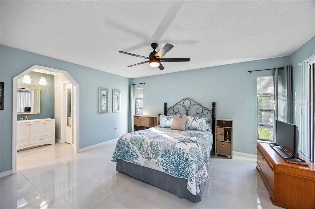 A bedroom with light blue walls, tile flooring, a queen bed, and an attached bathroom — 17341 HOLMES AVENUE, PORT CHARLOTTE, FL
