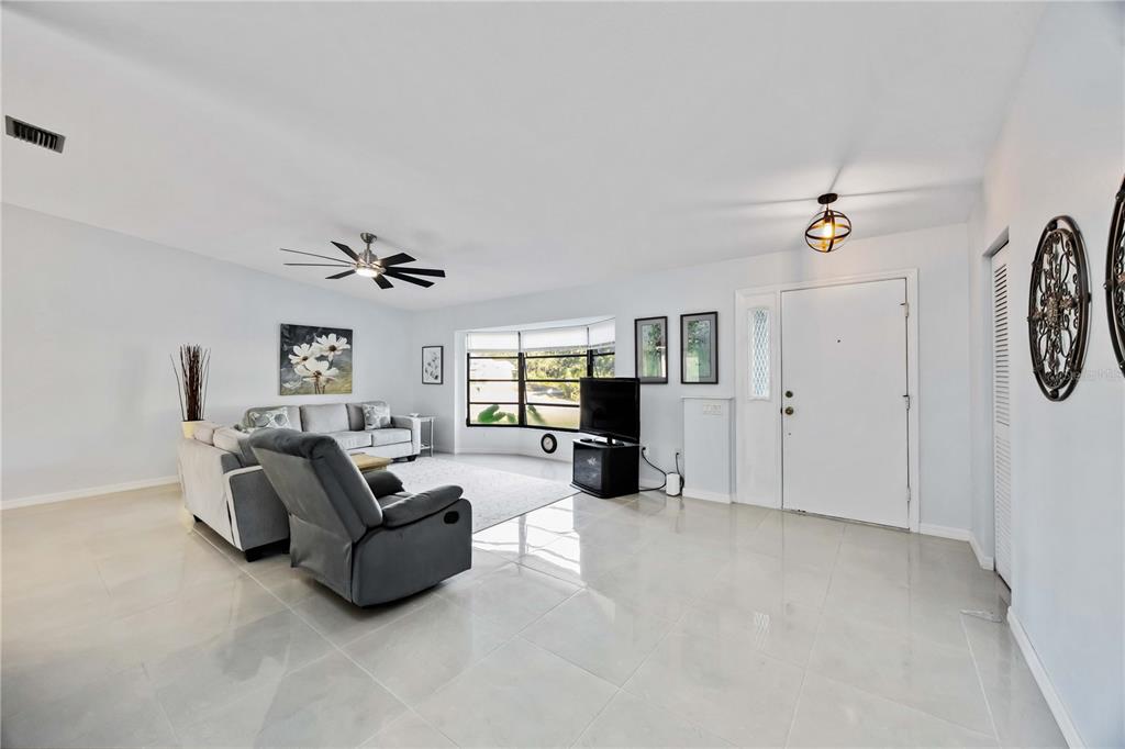 A bright living room features light tile floors, a gray sectional, and a large bay window — 17341 HOLMES AVENUE, PORT CHARLOTTE, FL