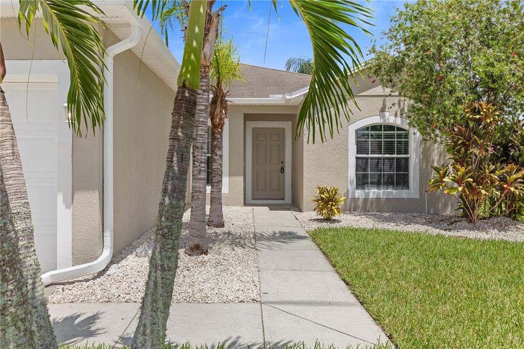A beige house exterior features a concrete walkway, palm trees, and a front entry door — 4611 CABALERRO TRAIL, KISSIMMEE, FL