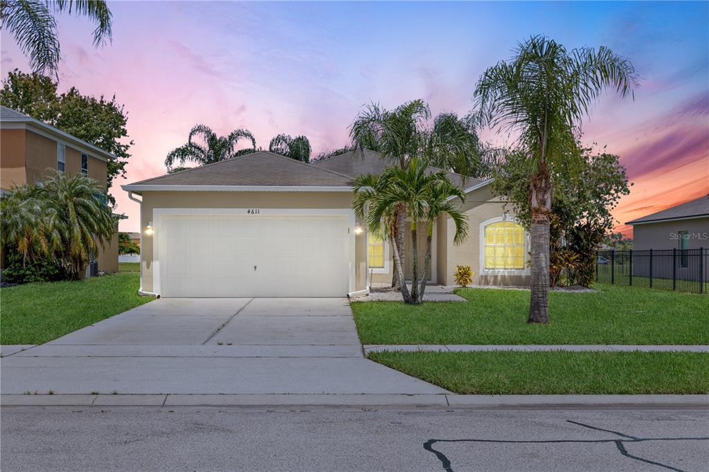 A single-story house with a two-car garage, palm trees, and a lawn at sunset — 4611 CABALERRO TRAIL, KISSIMMEE, FL