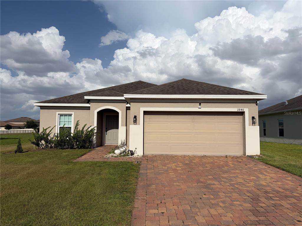 A single-story house with a tan stucco exterior, a two-car garage, and a brick driveway — 2840 WADEVIEW LOOP, ST CLOUD, FL