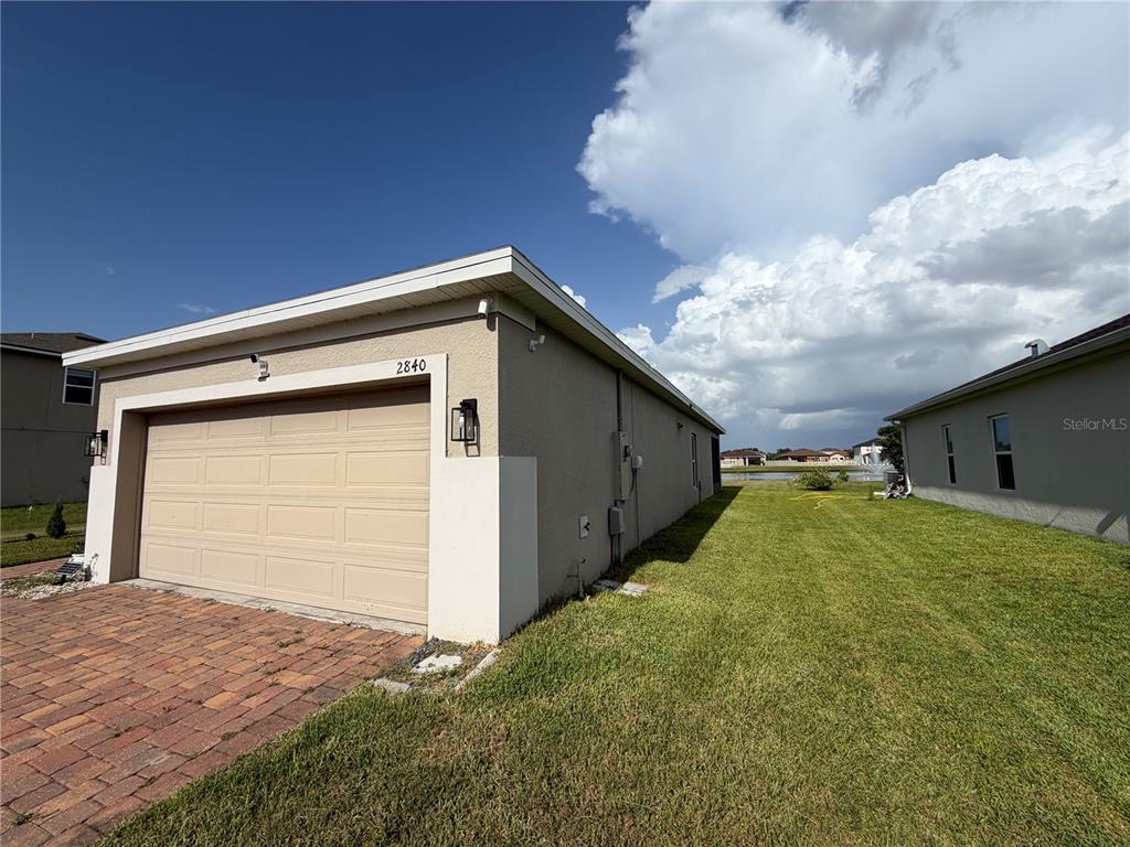 A tan house with a two-car garage and a side yard facing a pond — 2840 WADEVIEW LOOP, ST CLOUD, FL