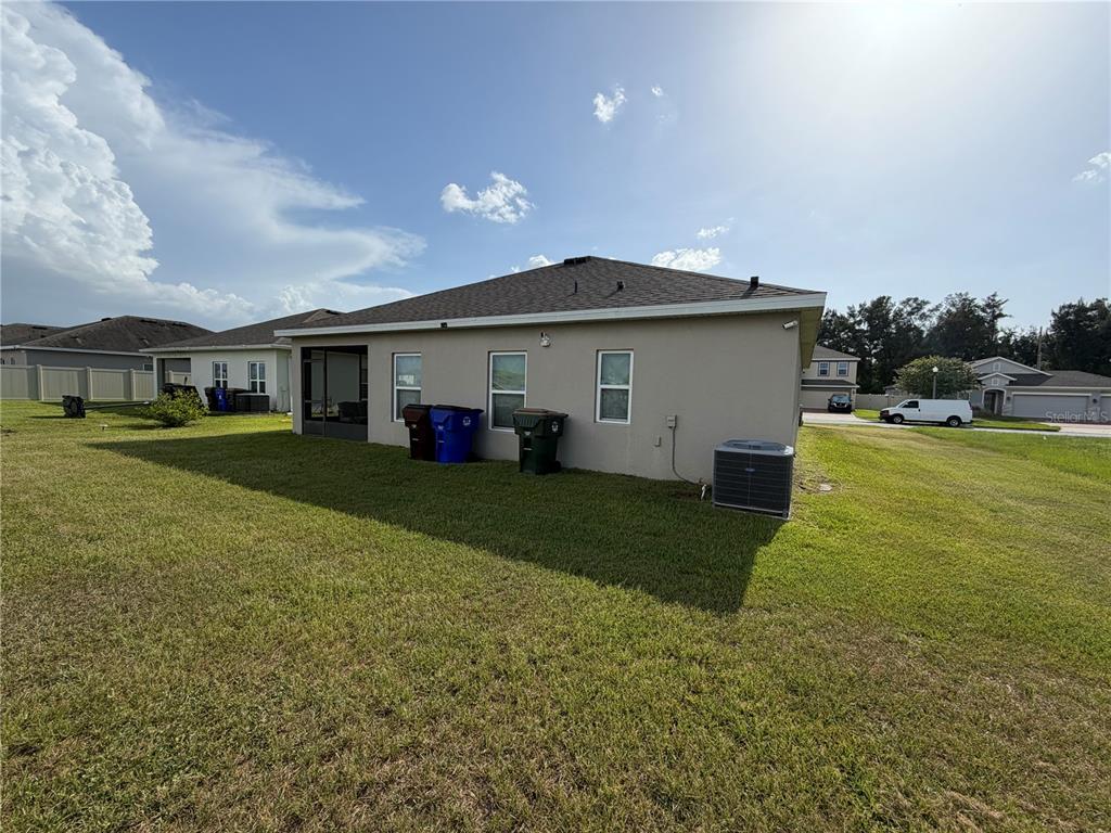 The rear exterior of a beige single-story house with a screened lanai and lawn — 2840 WADEVIEW LOOP, ST CLOUD, FL