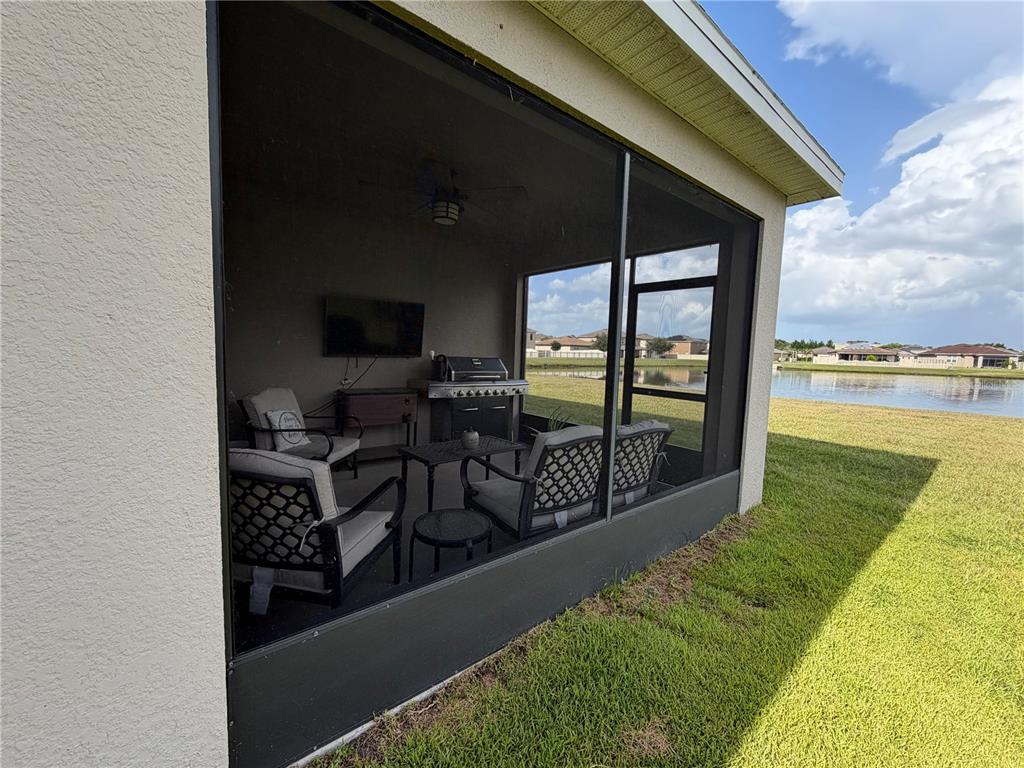 A screened-in patio features outdoor furniture, a grill, and a wall-mounted television overlooking a pond — 2840 WADEVIEW LOOP, ST CLOUD, FL