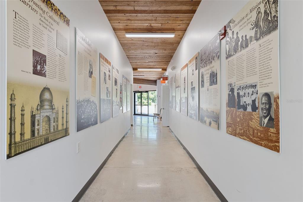 A long hallway features white walls lined with historical informational posters and a wood-paneled ceiling — 9300 UNIVERSITY BOULEVARD, ORLANDO, FL