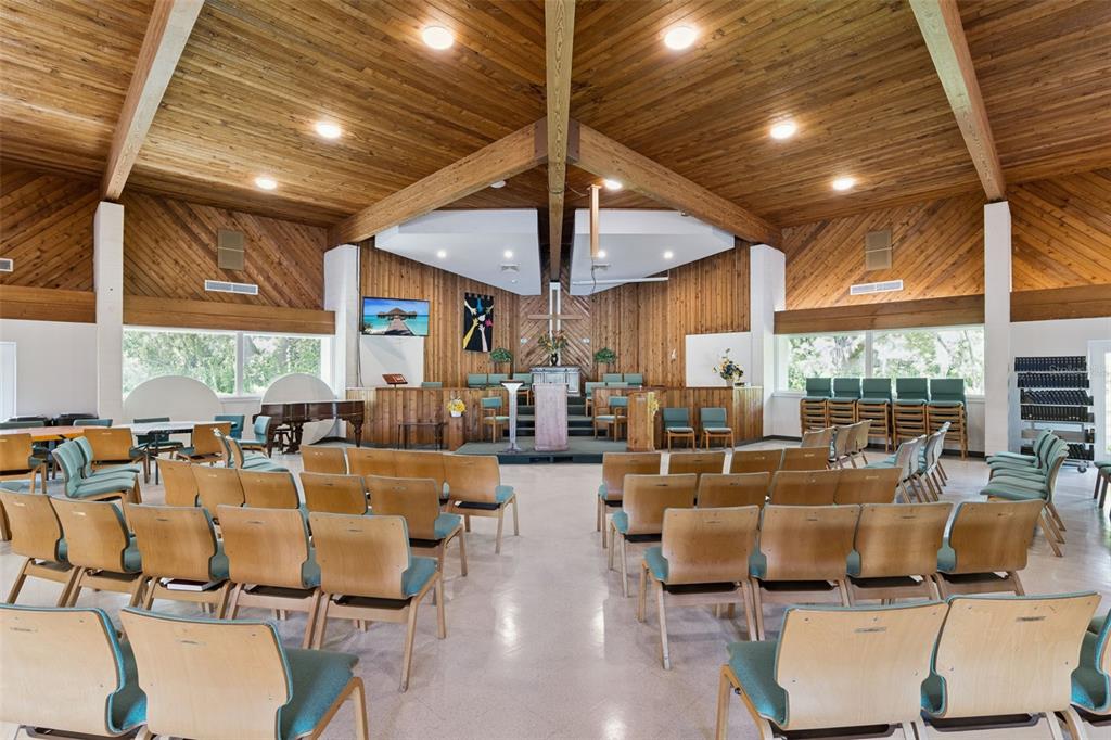 A church sanctuary features wood-paneled walls, a vaulted ceiling, and rows of chairs facing a stage — 9300 UNIVERSITY BOULEVARD, ORLANDO, FL
