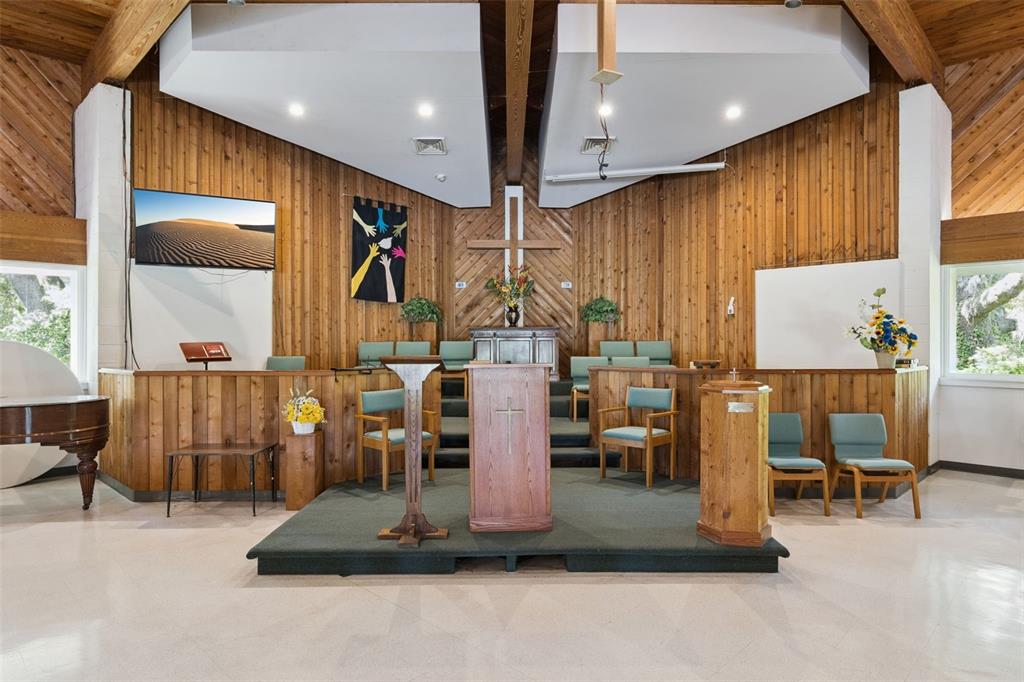 A church sanctuary features wood-paneled walls, a raised stage with a pulpit, and teal chairs — 9300 UNIVERSITY BOULEVARD, ORLANDO, FL