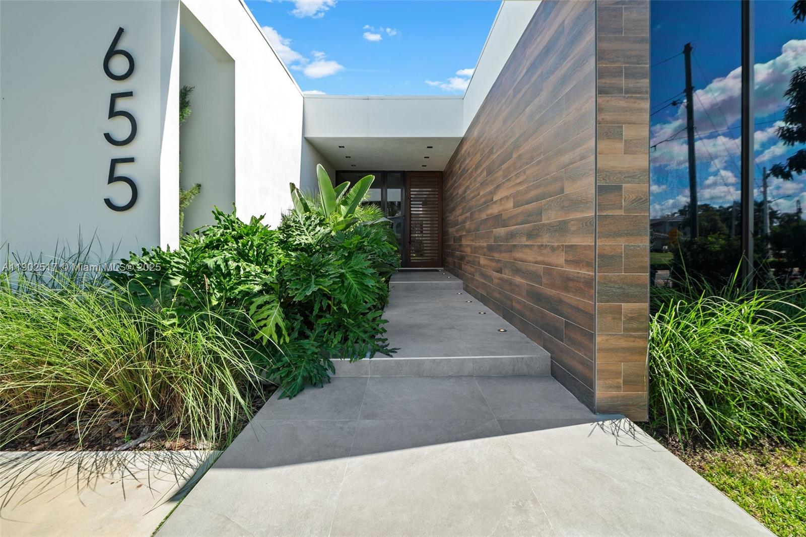 A modern home entrance features a tiled walkway, wood-look siding, and large house numbers — 655 Layne Blvd # 0, Hallandale Beach FL 33009, HALLANDALE BEACH, FL