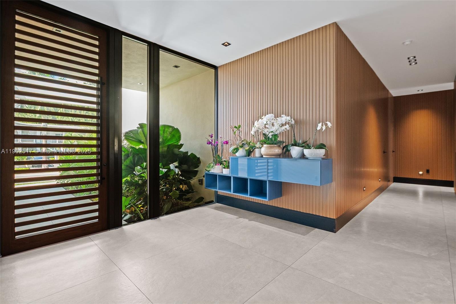 A modern entryway features light tile floors, wood-slatted walls, and a blue floating storage unit — 655 Layne Blvd # 0, Hallandale Beach FL 33009, HALLANDALE BEACH, FL