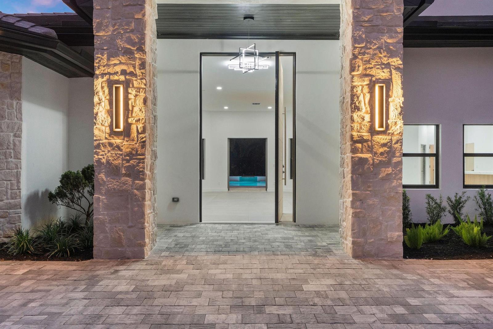 A modern home entrance features a large glass door flanked by stone pillars with sconces — 6451 Rodeo Drive, Southwest Ranches FL 33330, SOUTHWEST RANCHES, FL