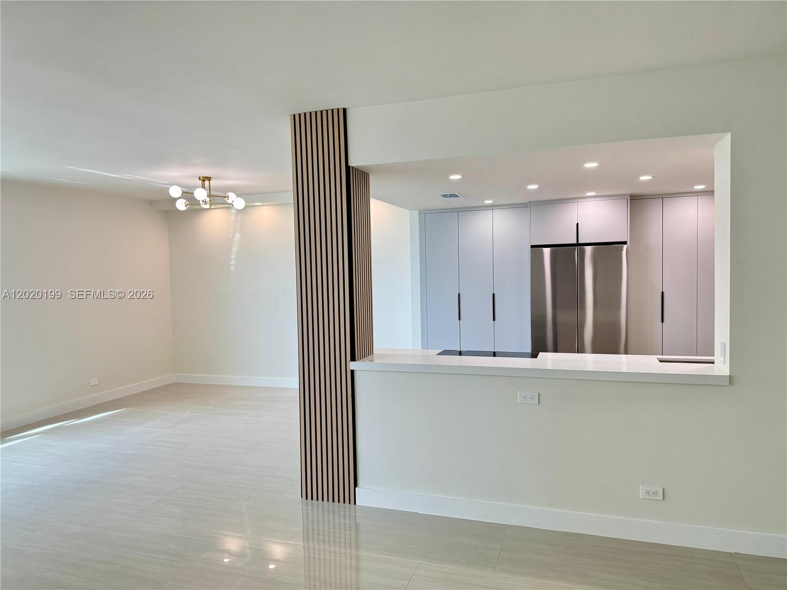 A modern kitchen with light cabinetry and a slatted wood accent wall overlooks a room — 5055 Collins Ave # 6F, Miami Beach FL 33140, MIAMI BEACH, FL