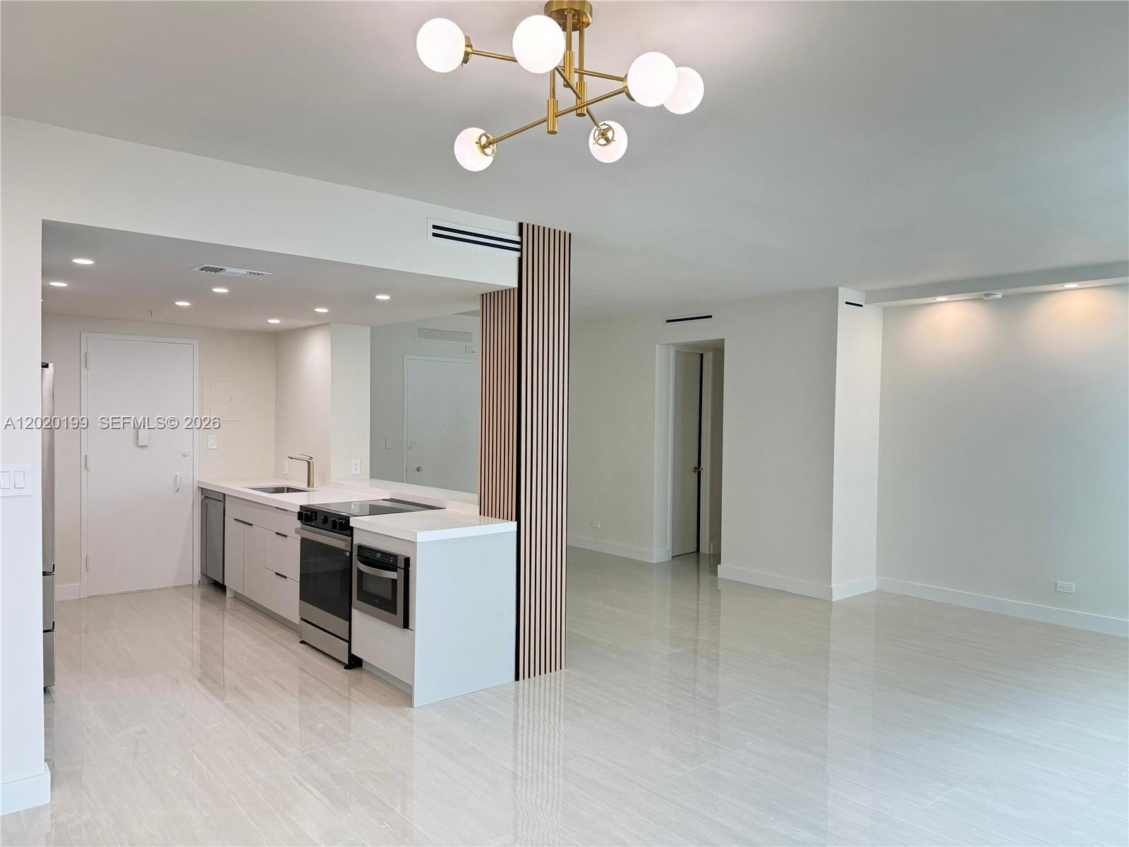 A modern kitchen with white cabinetry and a wood-slat accent wall opens to a living area — 5055 Collins Ave # 6F, Miami Beach FL 33140, MIAMI BEACH, FL