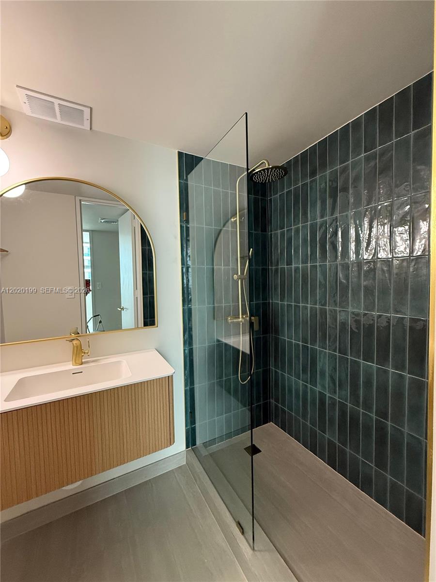 A modern bathroom features a glass-enclosed shower with dark green tiles and gold fixtures — 5055 Collins Ave # 6F, Miami Beach FL 33140, MIAMI BEACH, FL