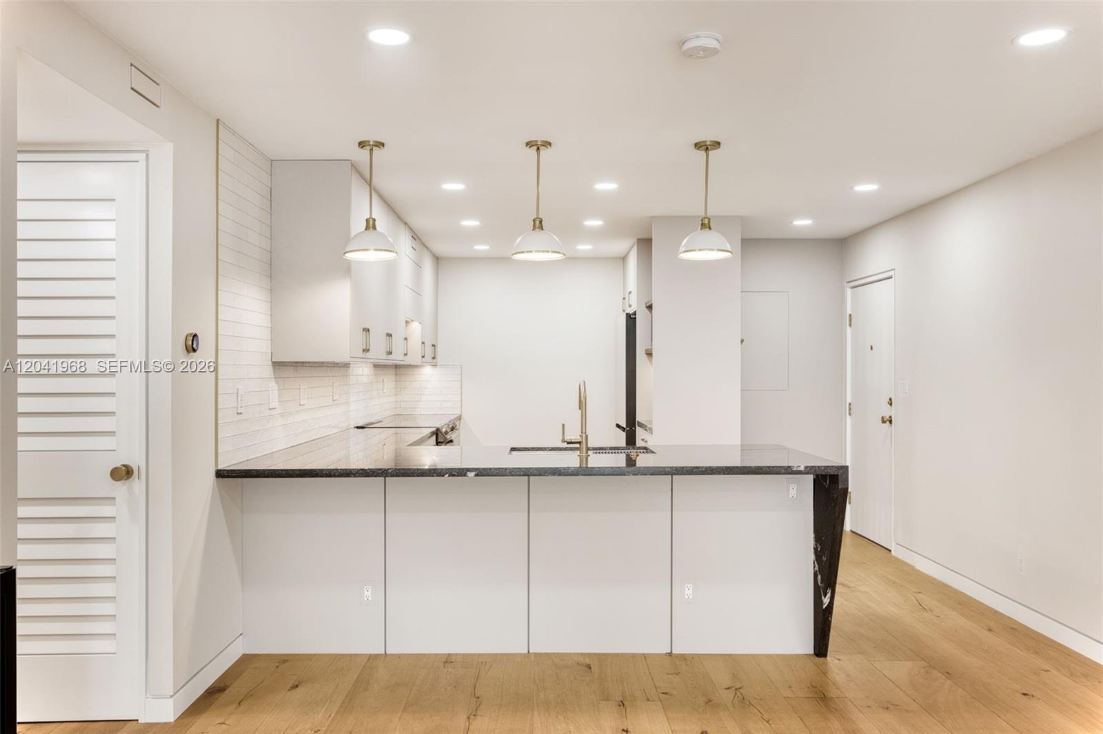 A modern kitchen features white cabinetry, a black marble-topped island, and light wood flooring — 100 Edgewater Dr # 142, Coral Gables FL 33133, CORAL GABLES, FL