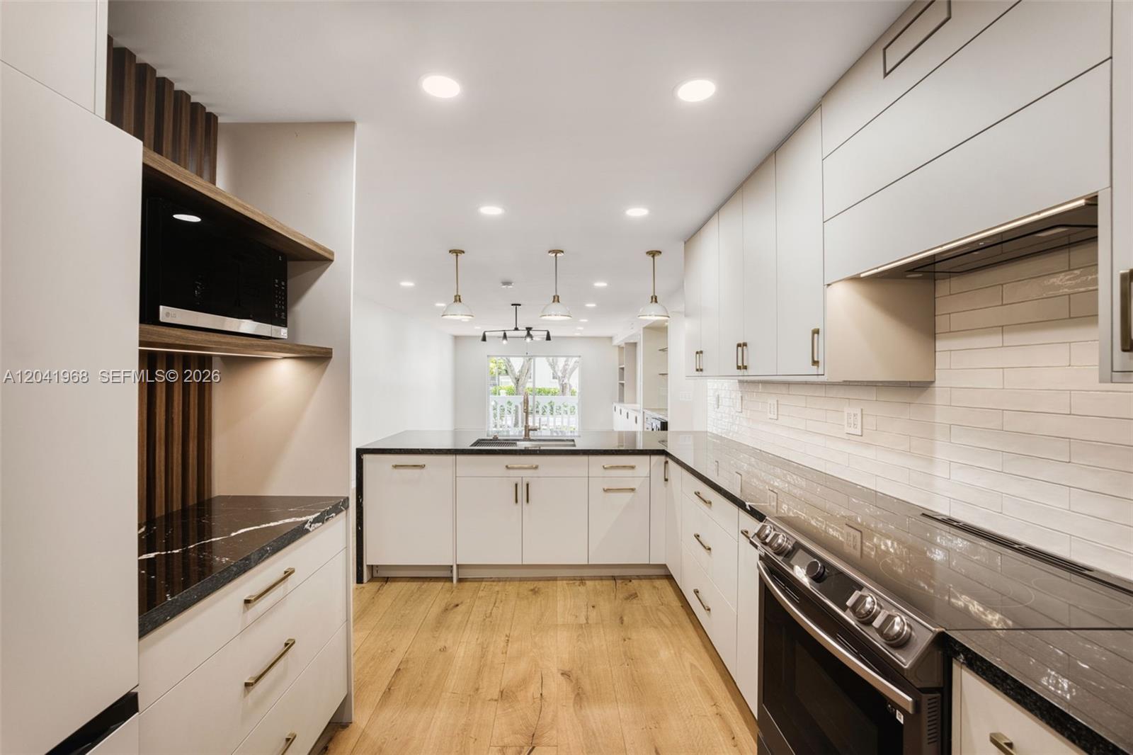 A modern kitchen features white cabinetry, black countertops, wood-look flooring, and recessed lighting — 100 Edgewater Dr # 142, Coral Gables FL 33133, CORAL GABLES, FL