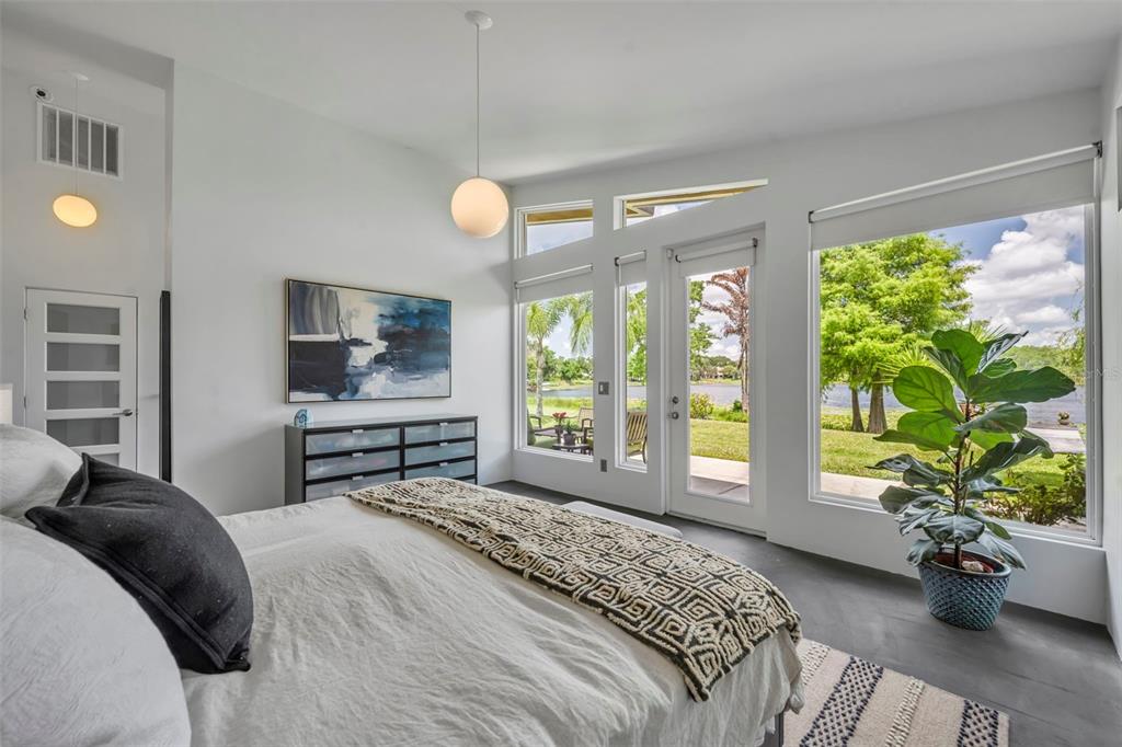 A modern bedroom features a bed, dresser, large windows, and a glass door overlooking water — 1841 LAKE SPIER DRIVE, WINTER PARK, FL
