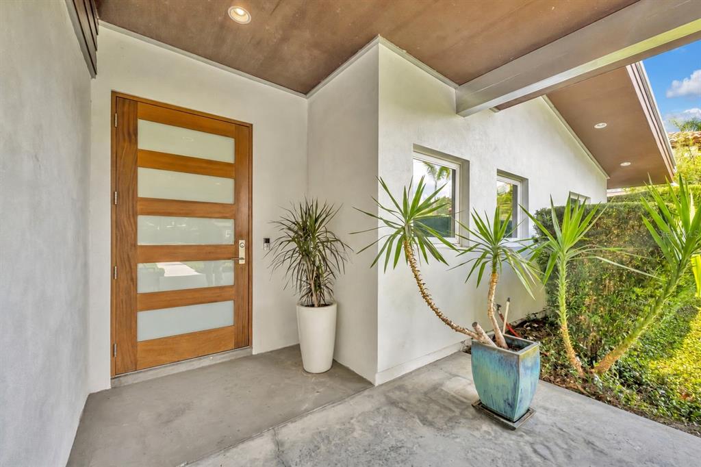 A modern front entryway features a wood door with frosted glass panels and potted plants — 1841 LAKE SPIER DRIVE, WINTER PARK, FL