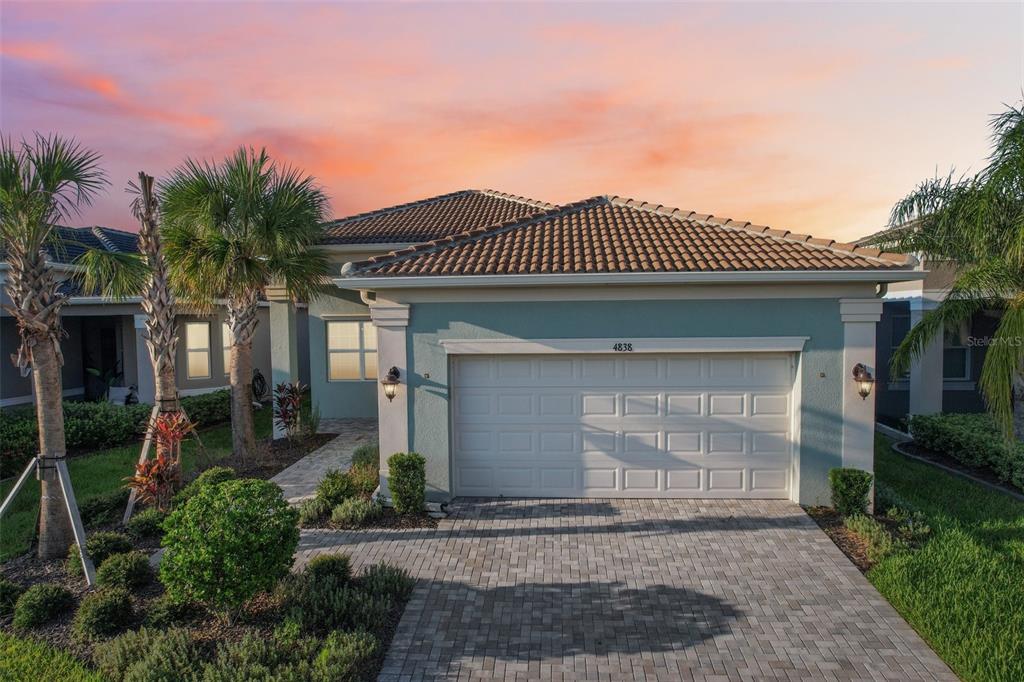 A light blue single-story house with a two-car garage and a paved driveway at sunset — 4838 SEVILLA SHORES DRIVE, WIMAUMA, FL
