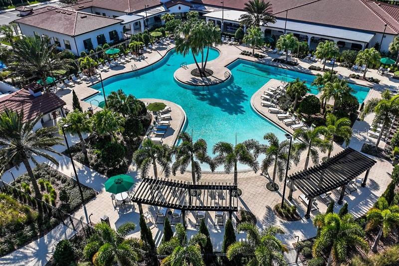 An aerial view shows a large swimming pool surrounded by lounge chairs and palm trees — 4838 SEVILLA SHORES DRIVE, WIMAUMA, FL