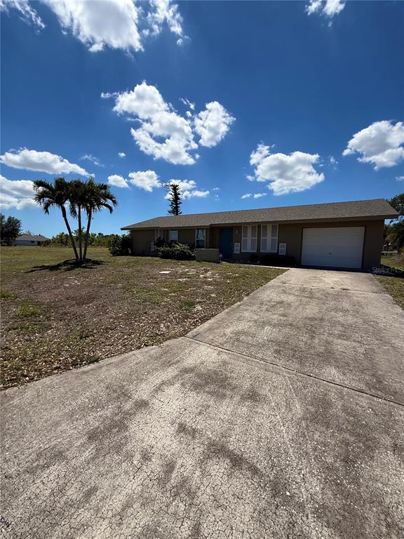 A single-story house with a concrete driveway, a garage, and a palm tree in front — 12884 BACCHUS ROAD, PORT CHARLOTTE, FL