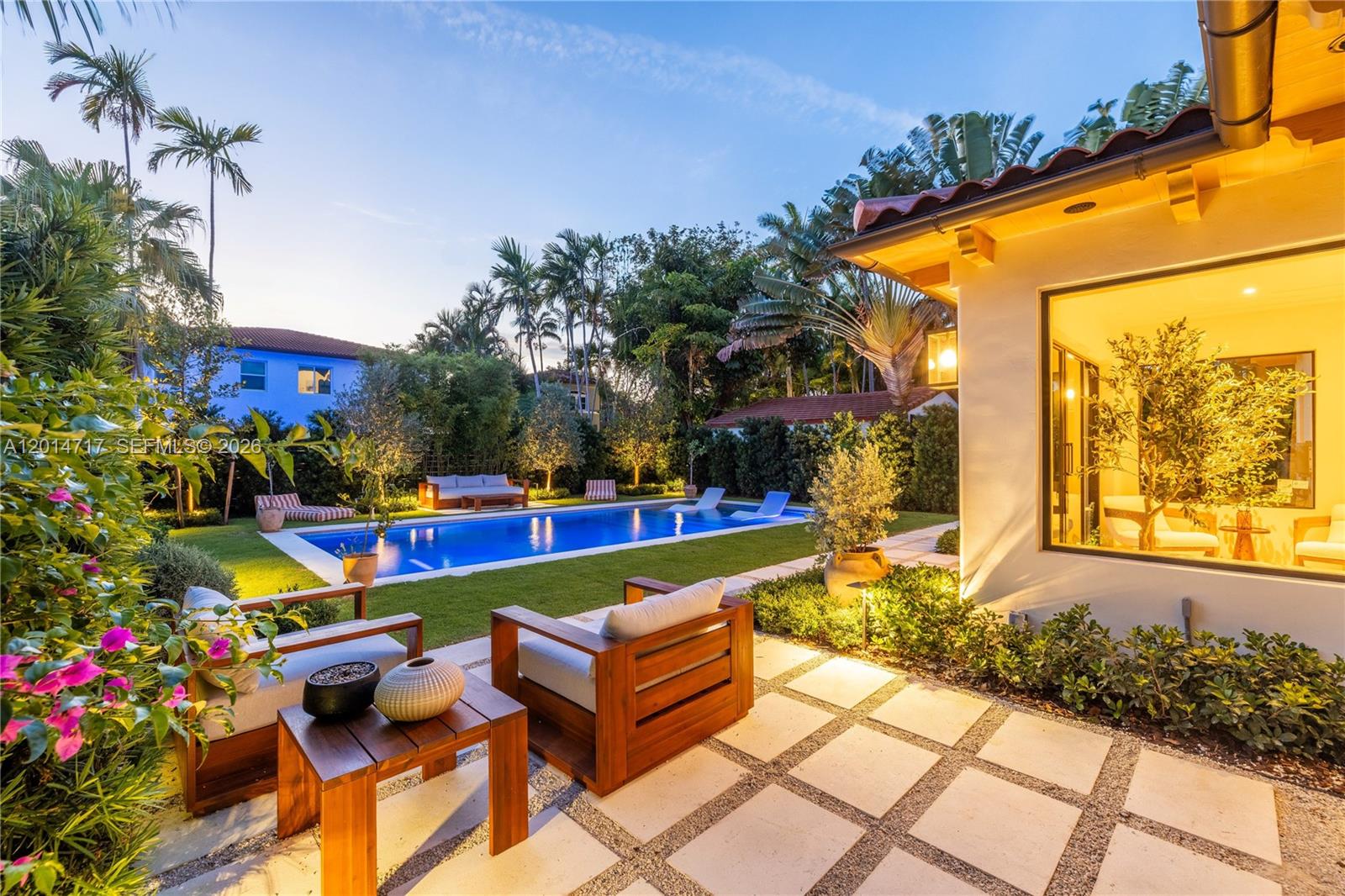 A backyard patio features a swimming pool, lounge chairs, and wooden seating at dusk — 4430 Royal Palm Ave, Miami Beach FL 33140, MIAMI BEACH, FL