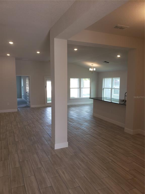 An open-concept living area features light wood-look tile flooring and a kitchen island — 4866 SUTHERLAND STREET Lot 62, SPRING HILL, FL
