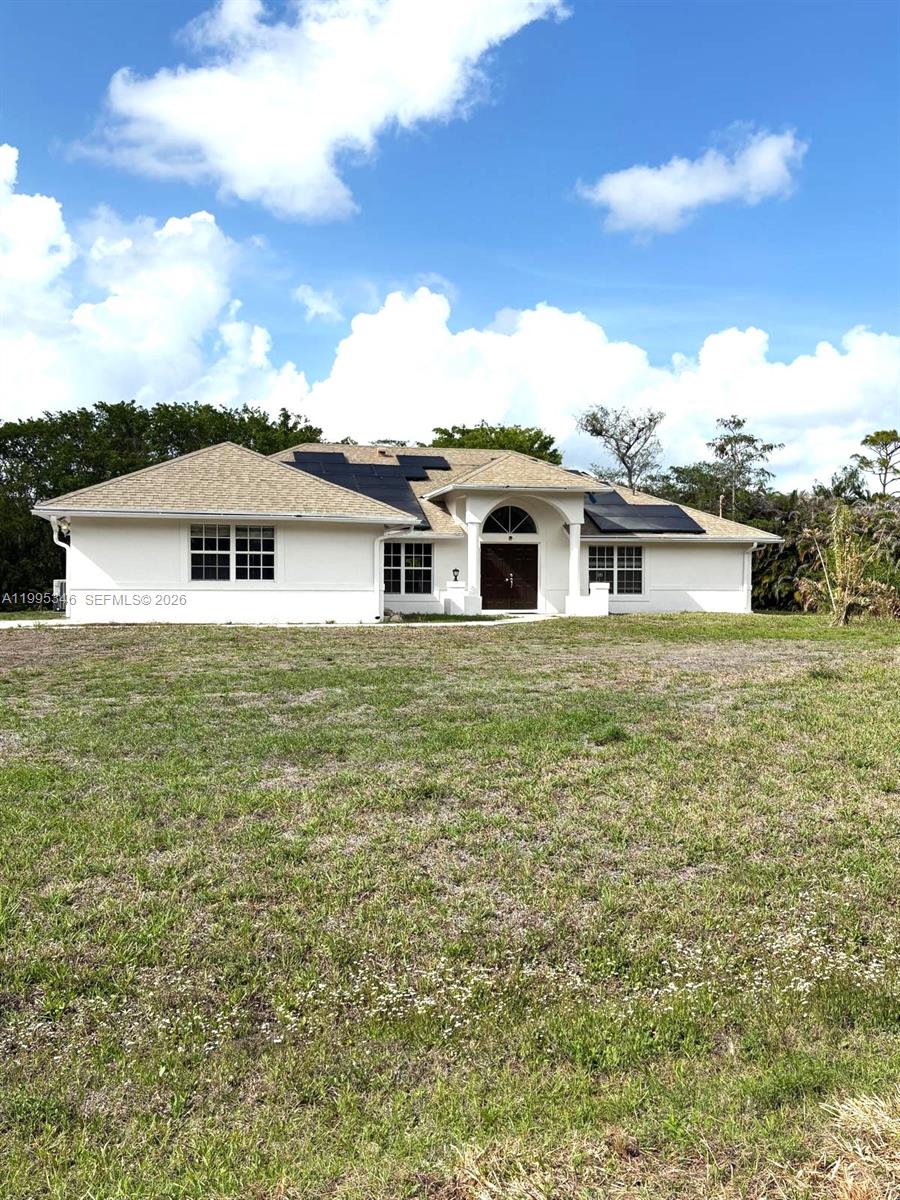 A single-story white house with a tan shingled roof and solar panels sits on grass — 16613 N 61st Pl N, Westlake FL 33470, WESTLAKE, FL