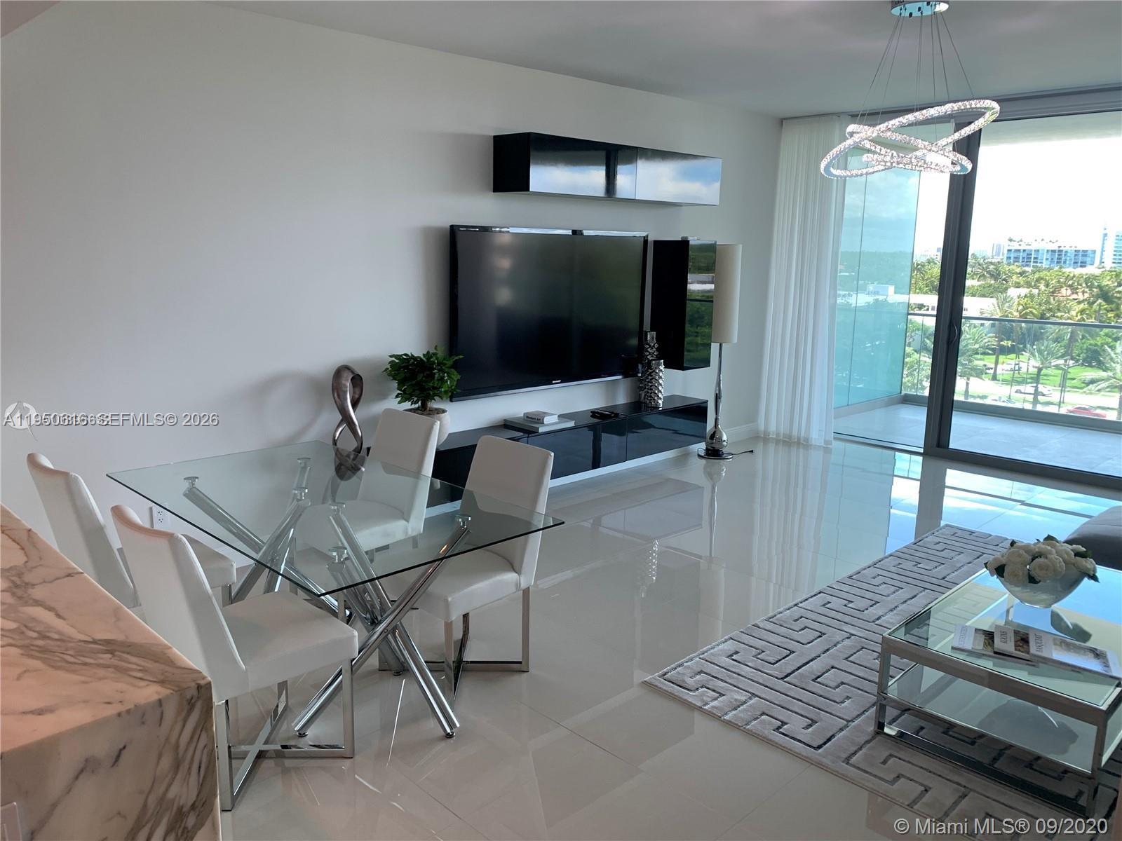 A modern living and dining area features white tile floors, glass furniture, and a balcony view — 10203 Collins Ave # 604, Bal Harbour FL 33154, BAL HARBOUR, FL