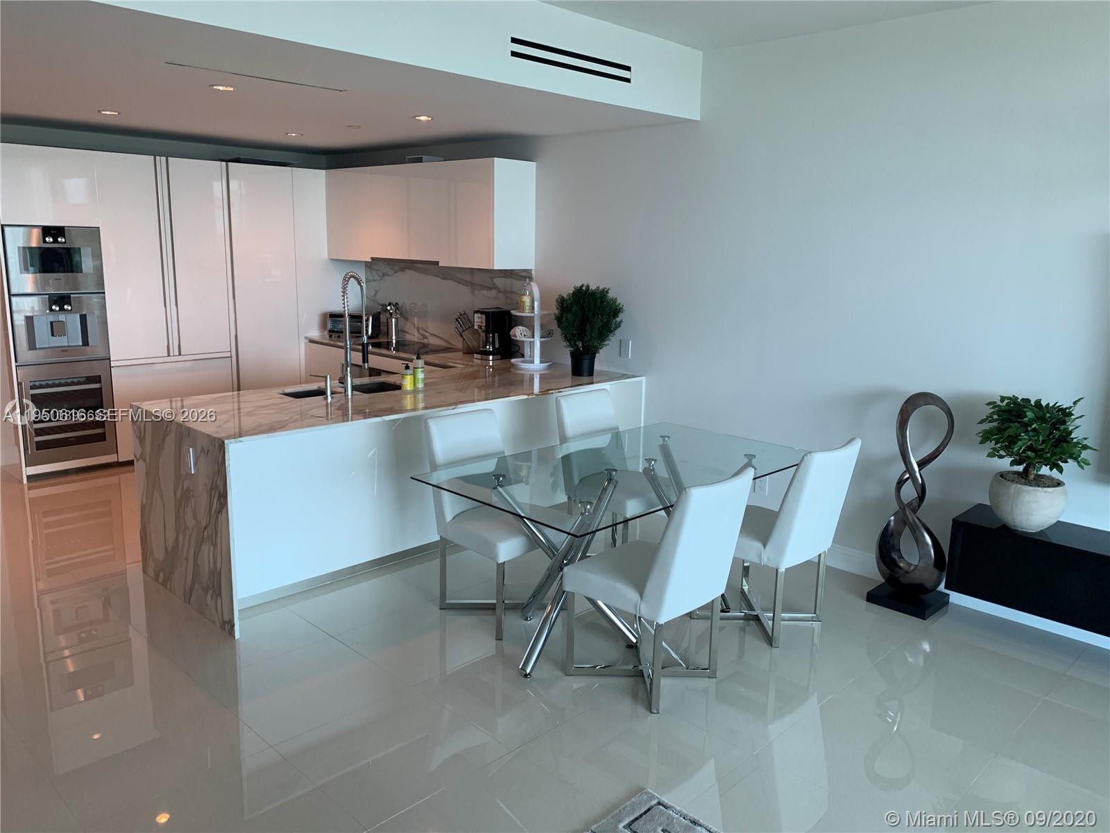 A modern kitchen features white cabinetry, marble countertops, and a glass dining table — 10203 Collins Ave # 604, Bal Harbour FL 33154, BAL HARBOUR, FL