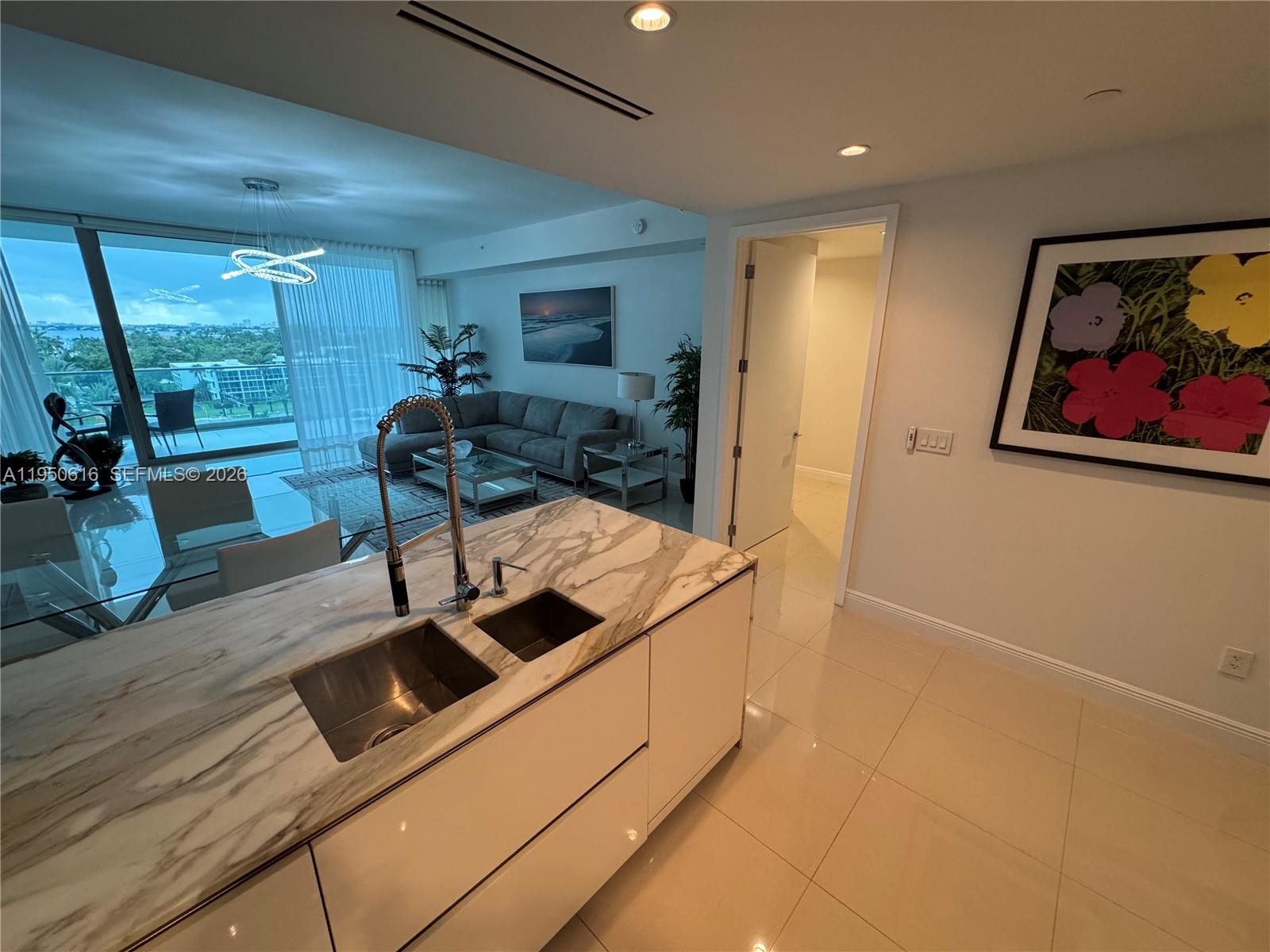 A modern kitchen island with a marble countertop sits before a living area and balcony — 10203 Collins Ave # 604, Bal Harbour FL 33154, BAL HARBOUR, FL