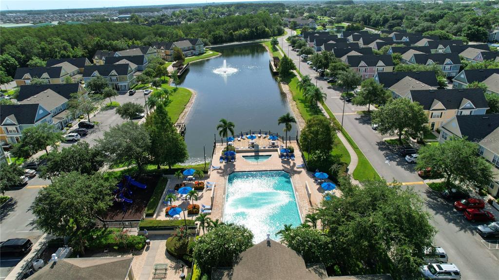An aerial view shows a community swimming pool, a lake with a fountain, and townhomes — 4009 VENETIAN BAY DRIVE UNIT 103, KISSIMMEE, FL