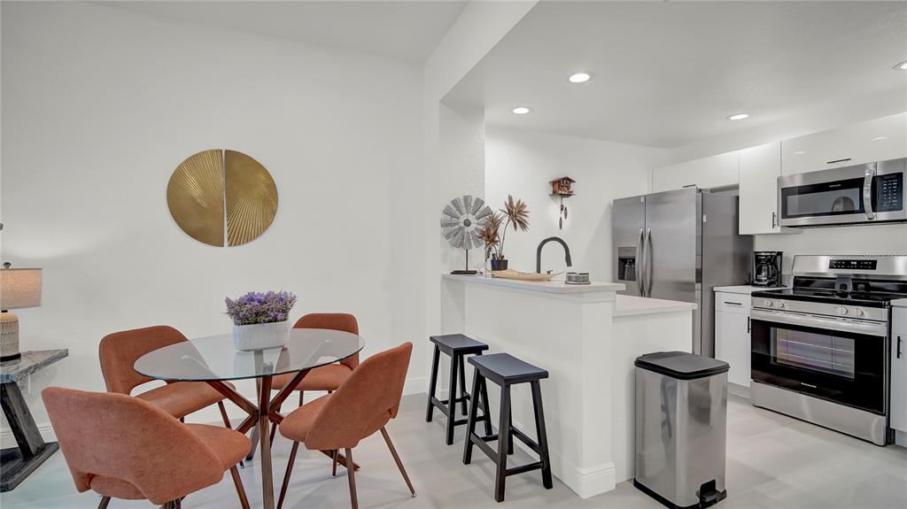 A dining area with a glass table and orange chairs sits beside a modern kitchen — 4009 VENETIAN BAY DRIVE UNIT 103, KISSIMMEE, FL
